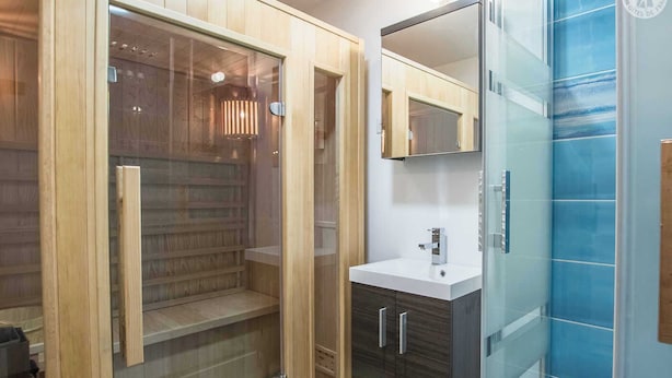 A modern bathroom with a glass-enclosed shower, a wooden vanity with a mirror, and a blue-tiled wall. - Chalet LES Violettes (LA PLAGNE TARENTAISE)