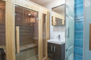A modern bathroom with a glass-enclosed shower, a wooden vanity with a mirror, and a blue-tiled wall.