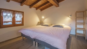 A bedroom with a bed, wooden beams, a window with lace curtains, and a shelf. - Chalet LES Violettes (LA PLAGNE TARENTAISE)