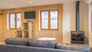 A cozy living room with a sofa, a television, a fireplace, and large windows. - Chalet LES Violettes (LA PLAGNE TARENTAISE)
