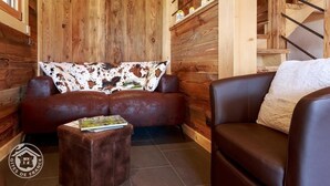 Una habitación acogedora con una pared de madera, un sofá de cuero marrón, un reposapiés a juego y una escalera al fondo.