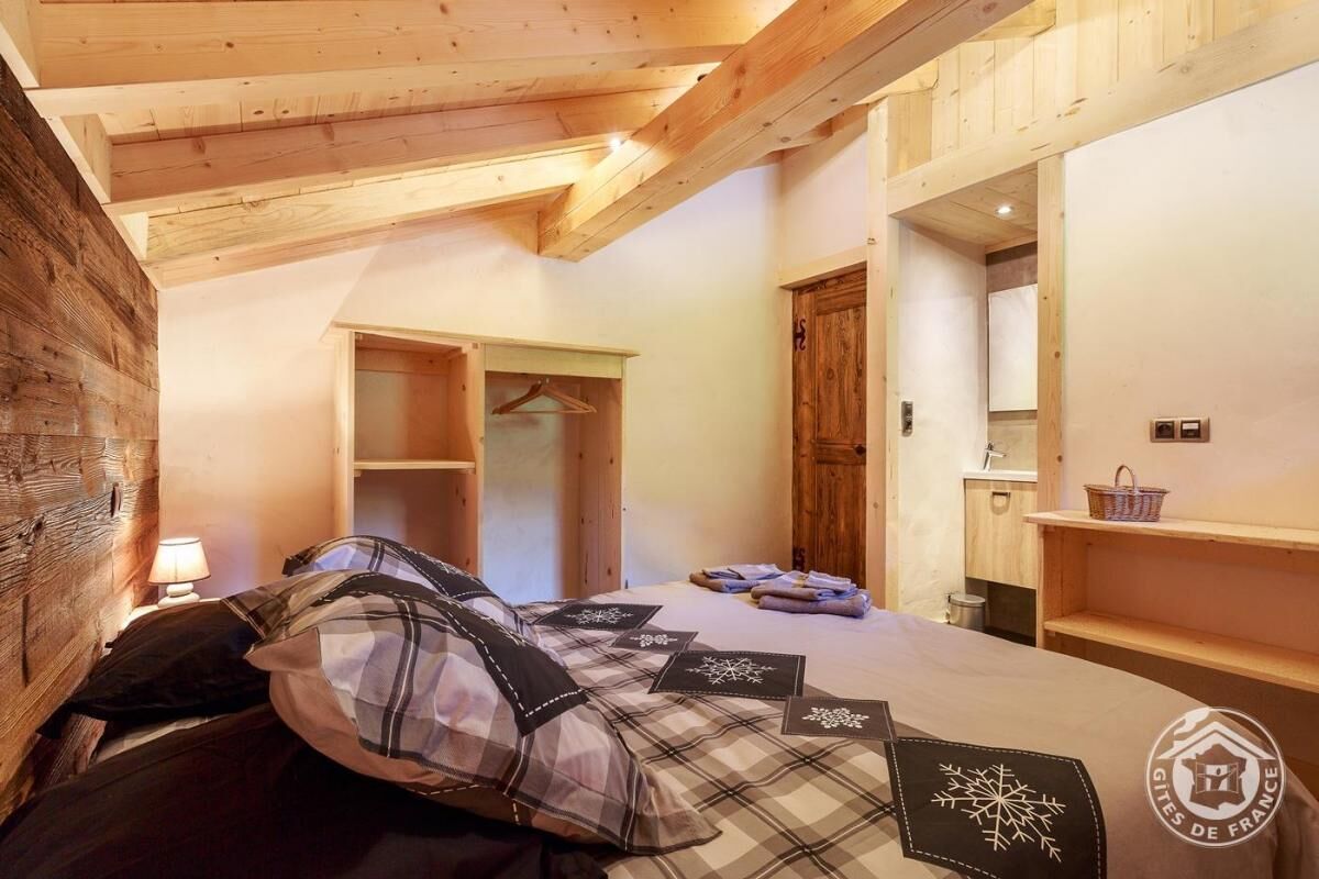 Ein gemütliches Schlafzimmer mit Holzboden, einem Bett mit Karo-Bettwäsche, einem Nachttisch mit Lampe und einem Holzschrank.
