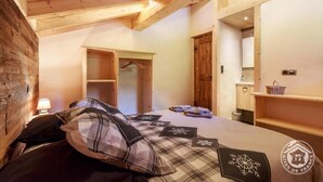 Un dormitorio acogedor con techo de madera, una cama con ropa de cama escocesa, una mesita de noche con lámpara y un armario de madera.