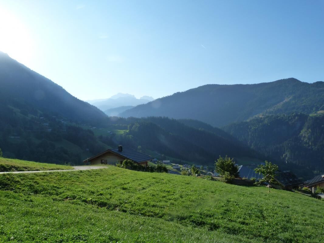 A rural landscape with a small house on a hill, surrounded by lush green fields and mountains in the background.