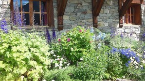 Ein Steinhaus mit Holzbalken und einem Garten voller verschiedener Blumen.