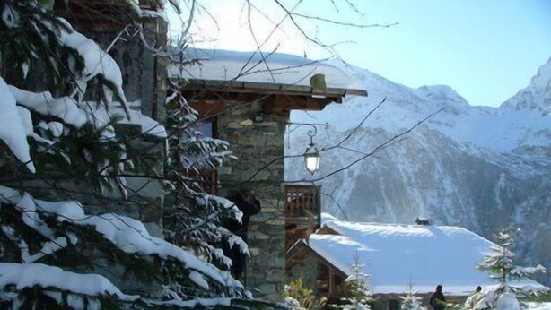 Ein schneebedecktes Berghotel mit Steinfassade, Holzbalken und einer Laterne.