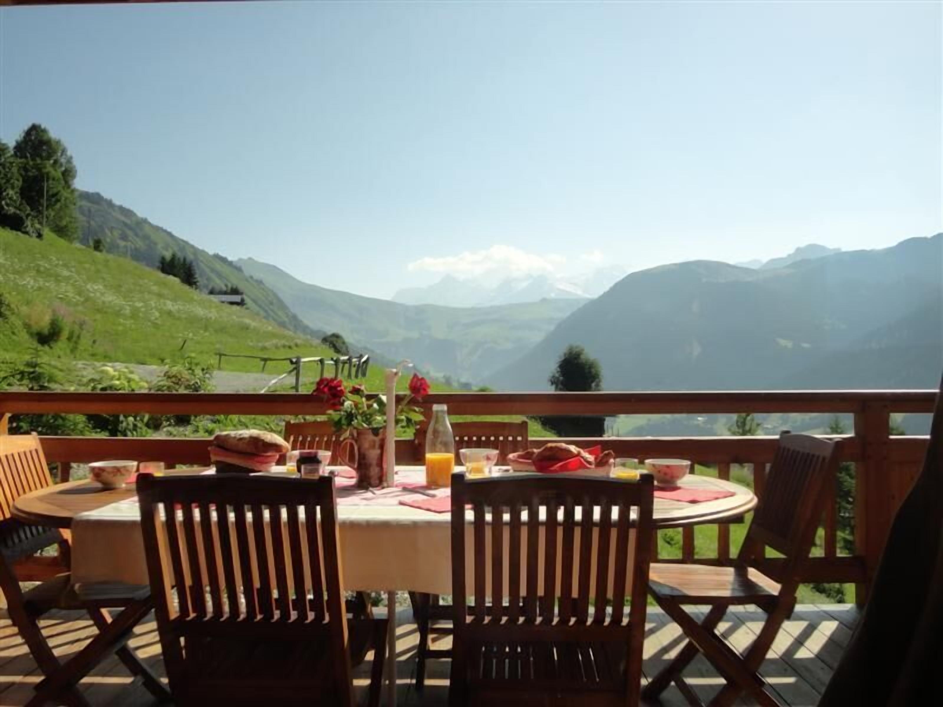 Eine Holzterrasse mit Tisch für zwei Personen, mit Blick auf eine Berglandschaft.
