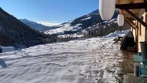 Un edificio de madera con suelo cubierto de nieve, un banco de madera y vistas a montañas nevadas.