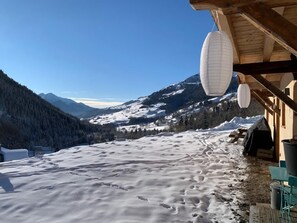 A wooden building with a snow-covered ground, a wooden bench, and a view of snow-capped mountains.
