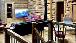 Interior de una cabaña de troncos con techo de madera, chimenea, televisor y sofá de cuero rojo.