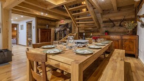 Un comedor de madera con una mesa larga dispuesta para una comida, vigas de madera en el techo y una escalera que lleva a un nivel superior.