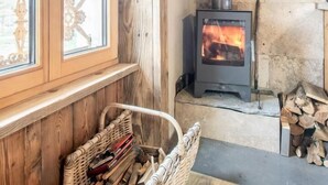 Una habitación acogedora con una estufa de leña, un ventanal con un tirador decorativo y una cesta llena de leña.