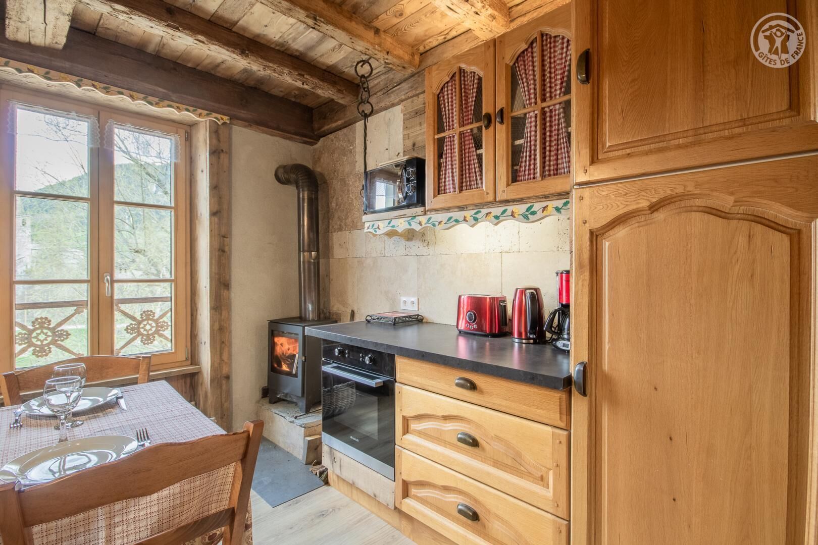 Une cuisine rustique avec des meubles en bois, un poêle à bois et un coin repas avec une table mise pour deux personnes.