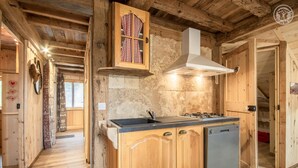 Una cocina de madera rústica con estufa empotrada, lavavajillas y ventana con cortinas de cuadros.