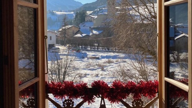 Una ventana con vistas a un paisaje nevado, que incluye casas y montañas.