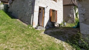 Une maison en pierre avec un toit en pente, des volets en bois et un petit porche à l’avant.