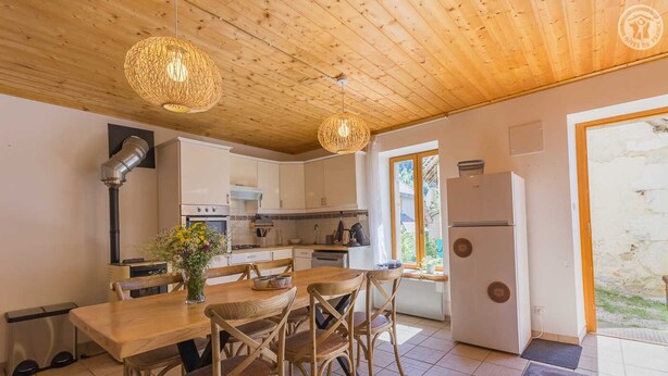 Une cuisine avec un plafond en bois, des armoires blanches, une table à manger avec des chaises et un réfrigérateur.