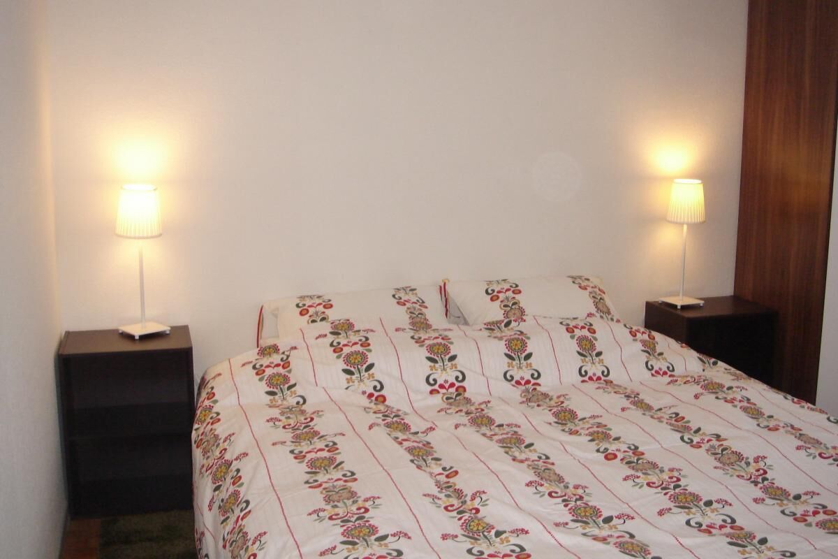 Un dormitorio con una cama, dos mesitas de noche y dos lámparas de pared.