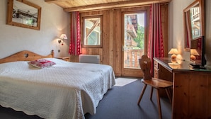 Een gezellige slaapkamer met een houten plafond, een bed met een witte quilt, een bureau met een lamp en een raam met rode gordijnen.