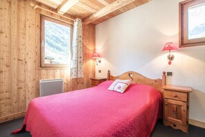 Una habitación de madera con una cama, una mesita de noche, una lámpara y una ventana con cortinas.