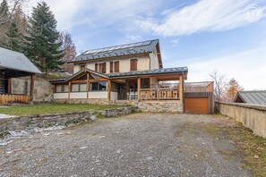 A two-story house with a stone foundation, wooden exterior, and a covered porch with outdoor seating. - L'ecoliere - Valmeinier (VALMEINIER)