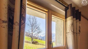 Une fenêtre donnant sur un arbre et des montagnes, des rideaux à motifs et un cadre en bois.