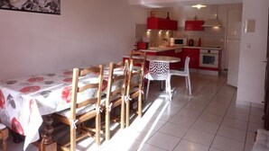 A dining area with a table and chairs, a kitchen in the background, and a ceiling light fixture. - Chez Desire - St-pierre-d'entremont (SAINT PIERRE D'ENTREMONT)
