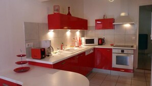 A modern kitchen with red cabinets, a white countertop, and a built-in oven. - Chez Desire - St-pierre-d'entremont (SAINT PIERRE D'ENTREMONT)