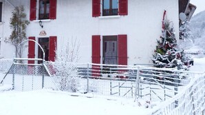 A white building with red shutters, a visible entrance, and a snow-covered fence. - Chez Desire - St-pierre-d'entremont (SAINT PIERRE D'ENTREMONT)