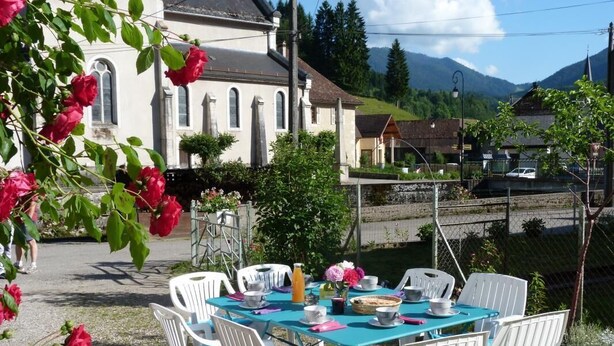 An outdoor dining area with white plastic chairs and a turquoise table set with plates, cups, and a basket. - Chez Desire - St-pierre-d'entremont (SAINT PIERRE D'ENTREMONT)