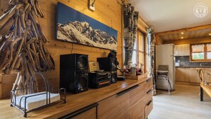 Une cuisine en bois avec un tableau représentant une montagne, un meuble en bois, un évier et une fenêtre avec des rideaux.