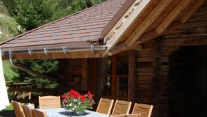 Une cabane en bois dotée d’un patio couvert, d’une table à manger avec des chaises et d’un vase à fleurs.