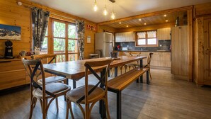 Un intérieur en bois comprenant une table et des chaises, un coin cuisine et une grande fenêtre avec des rideaux.