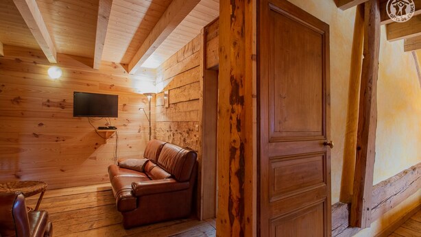 Interior de una cabaña de madera con un sofá de cuero, un televisor montado y una puerta de madera.