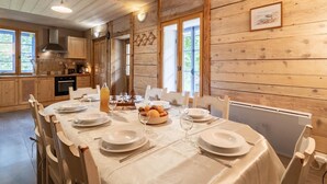 Interior de una cabaña de madera con una mesa de comedor para cuatro personas, rodeada de paredes de madera y ventanas amplias.
