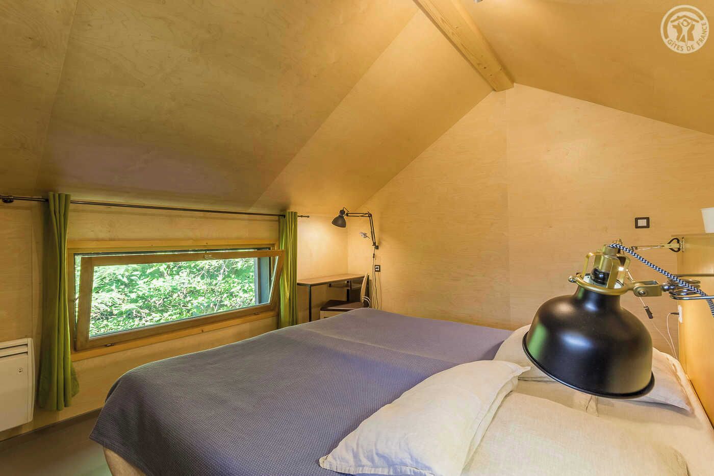 A bedroom with a single bed, a window with curtains, a desk with a lamp, and a radiator.