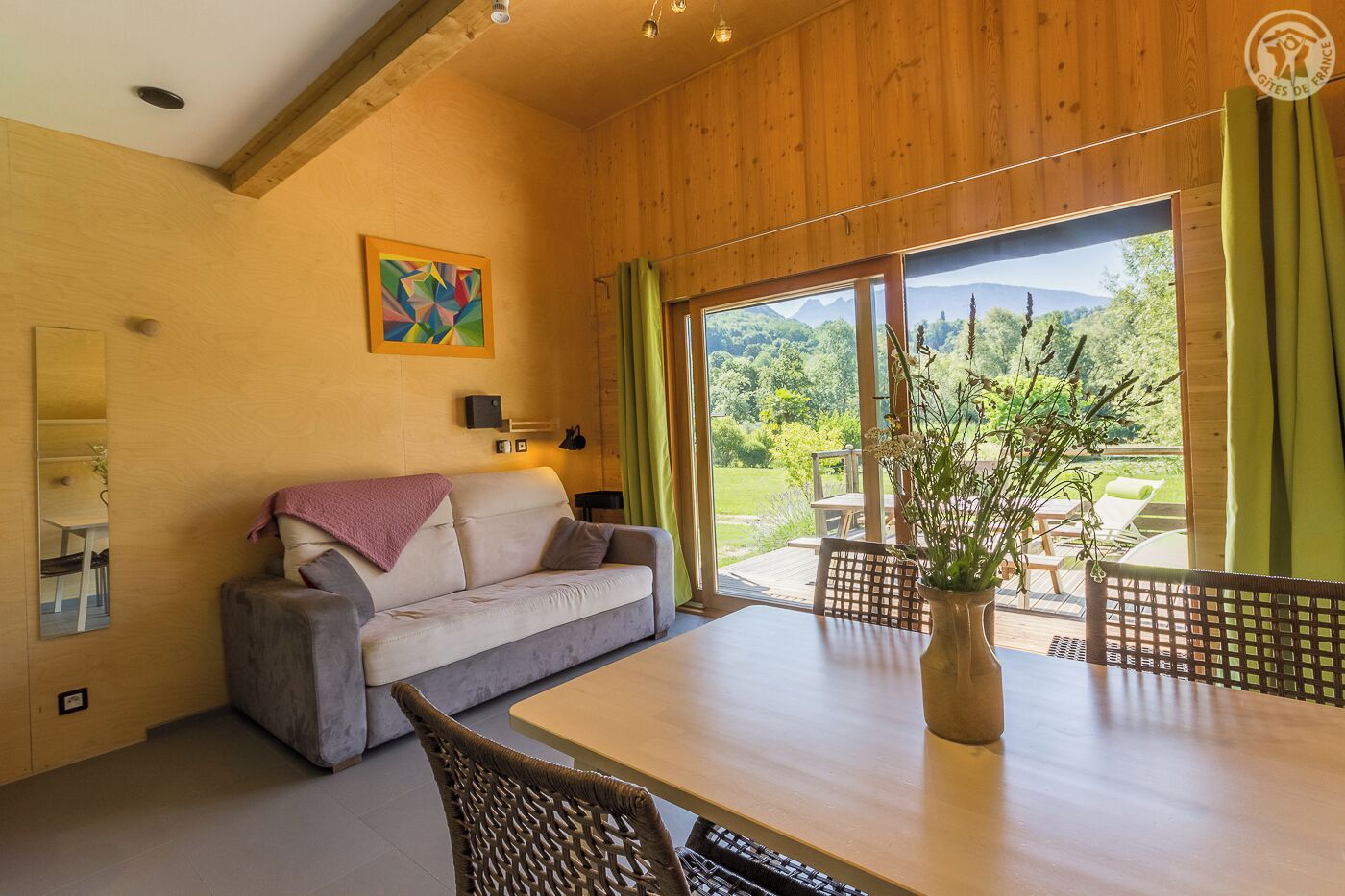 Ein gemütliches Zimmer mit einer Couch, einem Esstisch und einem großen Fenster mit Blick auf Grünflächen und Berge.