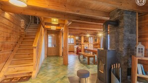 Interior de una cabaña de madera con escalera, chimenea y comedor.
