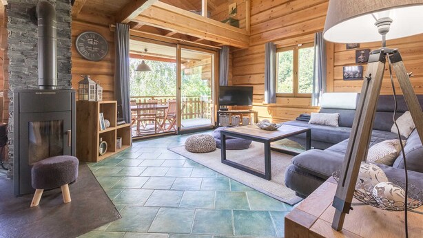 Interior acogedor de una cabaña con chimenea de piedra, mobiliario de madera y un ventanal con vistas a una terraza.