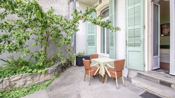Eine kleine Terrasse im Freien mit Tisch und Stühlen, eine Steinmauer und ein Gebäude mit grünen Fensterläden.