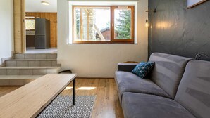 A modern living room with a grey sofa, a wooden coffee table, and a large window with a view of a stone building. - LA Cachette - Val-cenis (VAL CENIS)