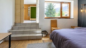 A bedroom with a bed, a window with a view of trees, a chair, and a staircase leading to another room. - LA Cachette - Val-cenis (VAL CENIS)
