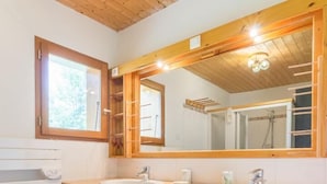 Une salle de bain avec un plafond en bois, un grand miroir, deux lavabos, des étagères en bois et un tapis rouge.
