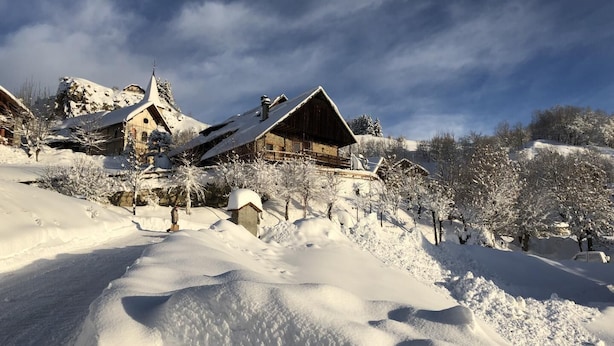 Un village de montagne enneigé, avec ses bâtiments traditionnels en bois, un ciel dégagé et une piste de ski.