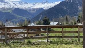Un paysage de montagne avec des sommets enneigés et une clôture en bois au premier plan.