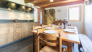 Une table de salle à manger en bois, mise avec des assiettes, des verres et des couverts, un mur en pierre et une cuisine avec des armoires en bois et un comptoir noir.