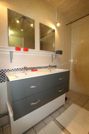 A bathroom with a large vanity, two mirrors, a sink, and a shower area.
