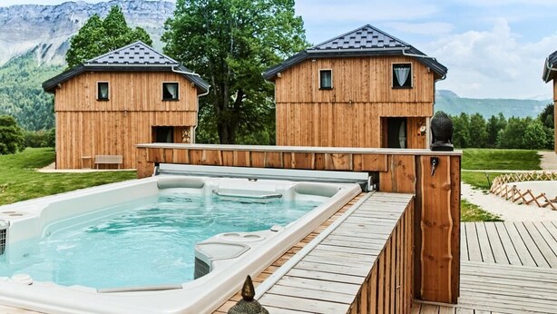 Una baita di legno con vasca idromassaggio e terrazza, immersa in un paesaggio montano.