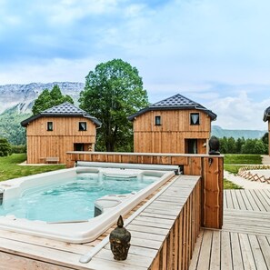 A wooden cabin with a hot tub and a deck, surrounded by a mountainous landscape. - LE Skieur - LA Feclaz-les-deserts (LA FECLAZ LES DESERTS)