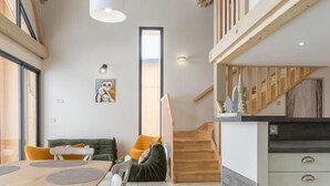 Un'ampia cucina con una scala in legno, un'area pranzo con tavolo e sedie, e un'ampia finestra che lascia entrare la luce naturale.